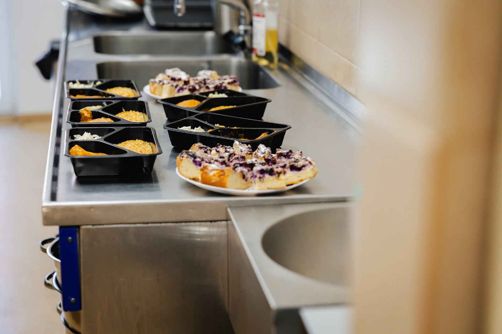 Maaltijdbakjes en gebak staan klaar op een roestvrijstalen keukenblad