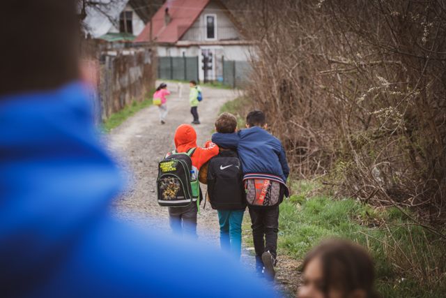 Kinderen met rugzakken lopen weg over een landweggetje in het dorp