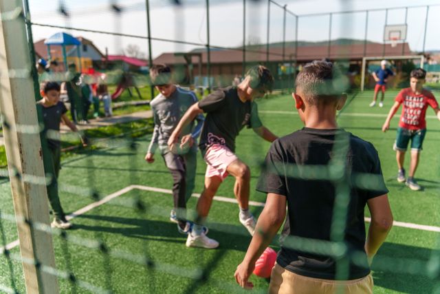 Kinderen voetballen op het kunstgrasveld, gezien door het net
